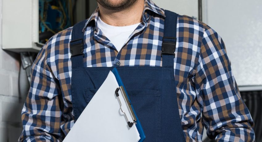 Electrician holding clipboard and smiling by electrical box